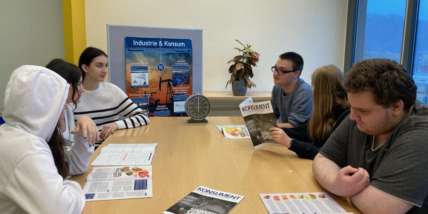 Schüler:innen an großem Tisch mit KONSUMENT-Heften