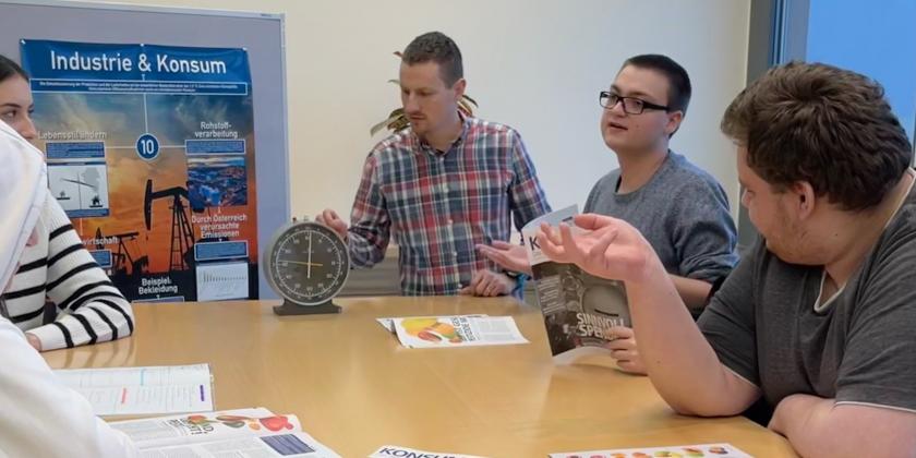 Schüler mit Lehrer an großem Tisch mit KONSUMENT-Heften