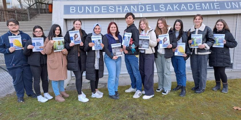 Klasse vor Schule mit KONSUMENT-Heften in der Hand
