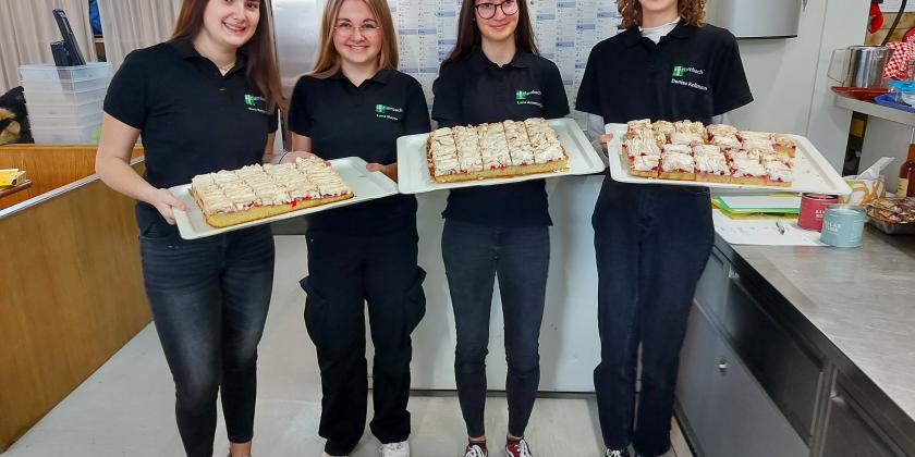 Schülerinnen zeigen Tabletts mit Speisen in der Küche