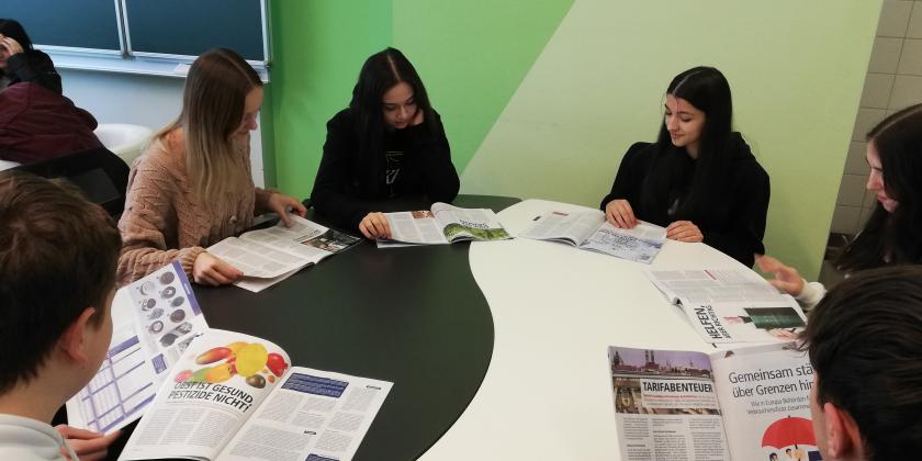 Schüler:innen an großem Tisch mit KONSUMENT-Heften