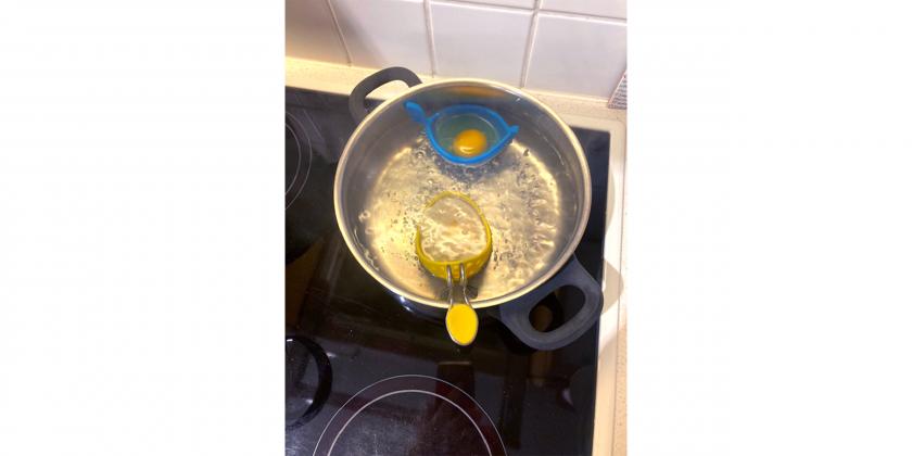 Cuisipro-Pochierer (gelb) und Egggondola (blau) eingehängt in den mit Wasser gefüllten Topf