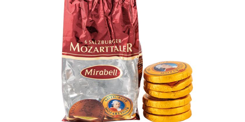 Mirabell Mozarttaler geöffnete leere Packung und daneben der Inhalt zum Größenvergleich