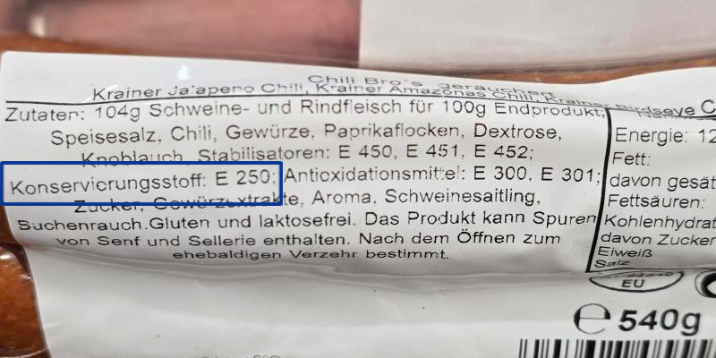 Zutatenliste einer Käsekrainer mit Makkaroni, versehen mit dem AMA-Gütesiegel. Blau hervorgehoben ist die Angabe „Konservierungsstoff: Natriumnitrit&amp;quot;.