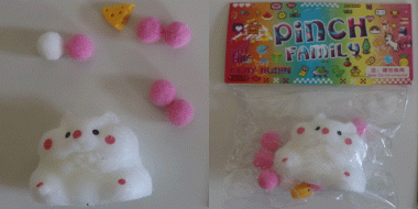 Weiße quetschbare Plüschfigur mit 5 rosa und 1 weißen kleinen Ball sowie einem kleinen Plastikkäsestück. Daneben dasselbe in Zellophan verpackt mit buntem verschließenden Karton oben