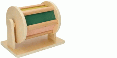 Ein hölzernes Montessori-Spielzeug in Form einer drehbaren Trommel auf einer rechteckigen Basis. Die Trommel besteht aus seitlichen runden Scheiben und mehreren bunten Lamellen in Grün, Rosa und Holzfarben. Sie ist auf zwei Stützen befestigt.