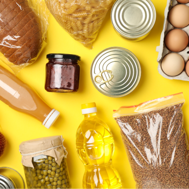 Verschiedene Lebensmittel, darunter Brot, Nudeln, Konserven, Öl, Eier, Erbsen im Glas und Buchweizen, auf gelbem Hintergrund