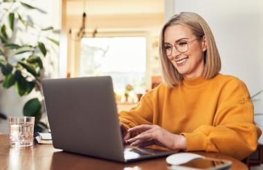 Eine Frau arbeitet am Laptop und lächelt.
