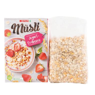 Der Beutelinhalt des Spar Müsli Jogurt-Erdbeere neben seiner Verpackung vor weißem Hintergrund. 