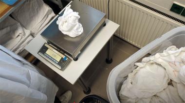 Wäsche abwiegen vor und nach dem Trocknen - Tisch mit Waage - darauf ein Wäschestück, Person steht vor dem Tisch