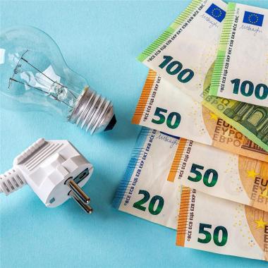 Glühbirne und Stromstecker liegen neben mehreren Euro-Geldscheinen auf hellblauem Hintergrund – Symbolbild für Stromkosten.