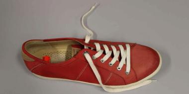 roter Ledersneaker mit 12 Ösen und weißem Schuhband auf blauem Untergrund