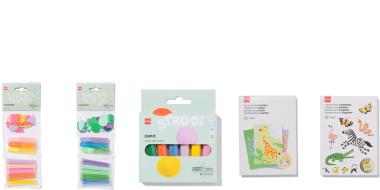 Fünf verschiedene Kinderprodukte in heller, freundlicher Verpackung. Links befinden sich zwei Sets bunter Strohhalme in Pastellfarben. Daneben liegt eine Packung mit farbigem Sand in mehreren kleinen Behältern. Rechts davon ist ein Set mit Tiermotiven für kreative Aktivitäten, unter anderem eine Giraffe. Ganz rechts befindet sich ein Stickerbogen mit verschiedenen Tieren wie Schmetterlingen, Zebra und Krokodil.