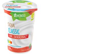 Weißer Becher „Vemondo Soja Classic“ der Marke Vemondo. Die Verpackung ist überwiegend weiß mit roten und blauen Akzenten. Auf der Vorderseite steht „SOJA CLASSIC“ sowie „OHNE ZUCKERZUSATZ“. Auf dem Deckel ist ebenfalls der Produktname sichtbar. Oben rechts befindet sich ein grünes veganes V‑Label. Der Becher fasst 500 g und wirkt wie ein veganer Joghurt auf Sojabasis.