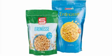 Zwei aufrecht stehende Beutel mit Erdnüssen vor weißem Hintergrund. Links befindet sich eine grüne Verpackung mit Punkten und großem Logo, darunter der Aufdruck „Erdnüsse“. Rechts steht ein höherer, blauer Beutel, ebenfalls mit der Bezeichnung „Erdnüsse“, dekoriert mit einer runden Abbildung gerösteter Nüsse. 
