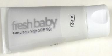 Auf dem Bild ist eine liegende Tube Sonnencreme zu sehen. Die Verpackung ist überwiegend weiß und schlicht gestaltet. Auf der Vorderseite steht der Markenname „fresh baby“ in grauer Schrift, darunter der Hinweis „sunscreen high SPF 50“. Rechts befindet sich ein kleiner, senkrecht ausgerichteter Aufdruck. Die Tube hat eine weiße, runde Verschlusskappe.