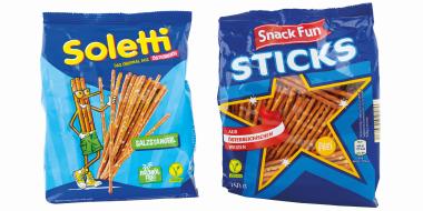 Zwei bunt gestaltete Snackpackungen mit Salzstangen vor weißem Hintergrund. Links befindet sich eine hellblaue Packung der Marke „Soletti“ mit einem gezeichneten Salzstangen-Maskottchen und einem Bild, das die dünnen, braunen Sticks zeigt. Rechts steht eine dunkelblaue Verpackung „Snack Fun Sticks“, mit Sichtfenster in Sternform, durch das die Salzstangen sichtbar sind. 