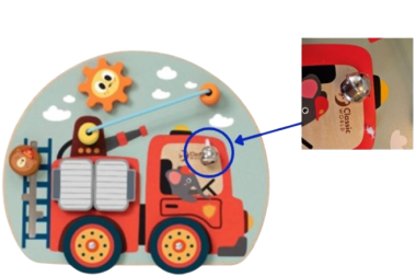 Ein buntes Holzspielzeug in Form eines Feuerwehrautos ist abgebildet. Auf dem Fahrzeug befinden sich verschiedene bewegliche Elemente wie Zahnräder und Schieber. Mit einem blauen Kreis und Pfeil wird eine kleine silberne Glocke hervorgehoben, die am Feuerwehrauto befestigt ist. Rechts zeigt eine vergrößerte Detailansicht die Glocke genauer.