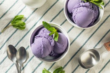 2 Eisschüsseln mit lila Eiskugeln auf weiß-grün gestreiftem Tischtuch, Löffel neben dem Eisbechern