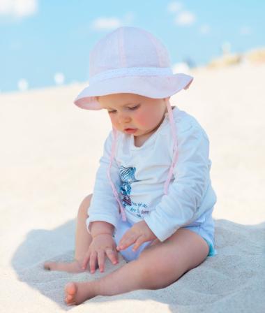 Baby sitzt im Schatten am Strand und spielt mit Sand