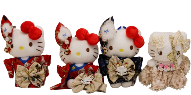 Vier Hello-Kitty-Plüschfiguren sind nebeneinander vor weißem Hintergrund angeordnet. Drei Figuren tragen traditionelle Kimonos in Rot, Blau und Dunkelblau mit großen dekorativen Schleifen und floralen Mustern. Die Schleifen am Kopf sind rot bzw. blau. Die vierte Figur trägt ein cremefarbenes Spitzenkleid mit Stoffblumen und Schleife. Alle Figuren besitzen Katzenohren, Schnurrhaare, schwarze Augen und eine gelbe Nase. Die Kleidung ist detailreich verziert und wirkt festlich sowie dekorativ.