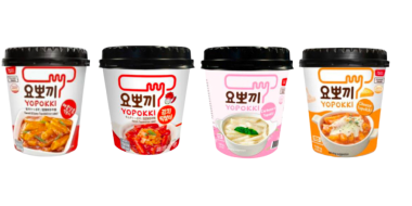 Das Bild zeigt vier Becher koreanischer Instant-Tteokbokki-Produkte der Marke Yopokki vor einem hellen Hintergrund. Die Verpackungen sind in unterschiedlichen Farben gestaltet und stehen für verschiedene Geschmacksrichtungen. Von links nach rechts sind Varianten mit brauner, roter, rosa und orangefarbener Kennzeichnung zu sehen. Jeder Becher besitzt einen schwarzen Deckel sowie Produktabbildungen der zubereiteten Speisen auf der Vorderseite. Die Anordnung ist symmetrisch und hebt die Produktvielfalt hervor.