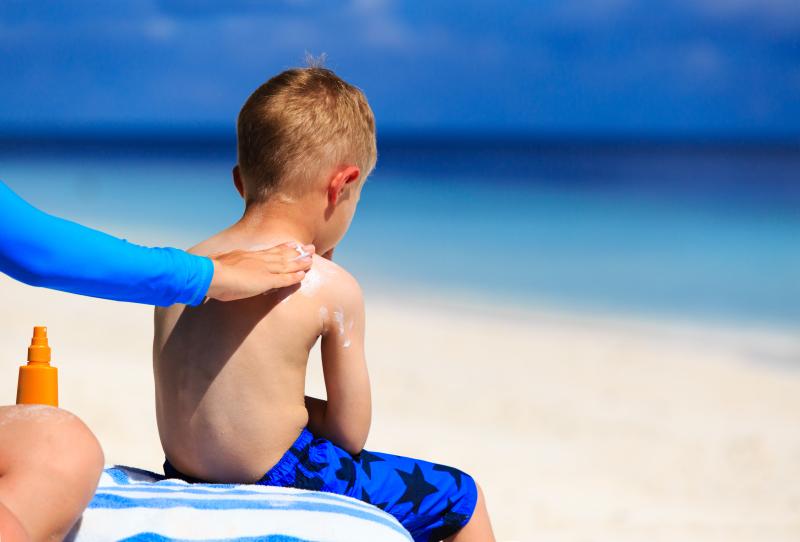 Kinder Sonnencreme Test: Kind sitzt am Strand Eltern tragen Sonnencreme auf