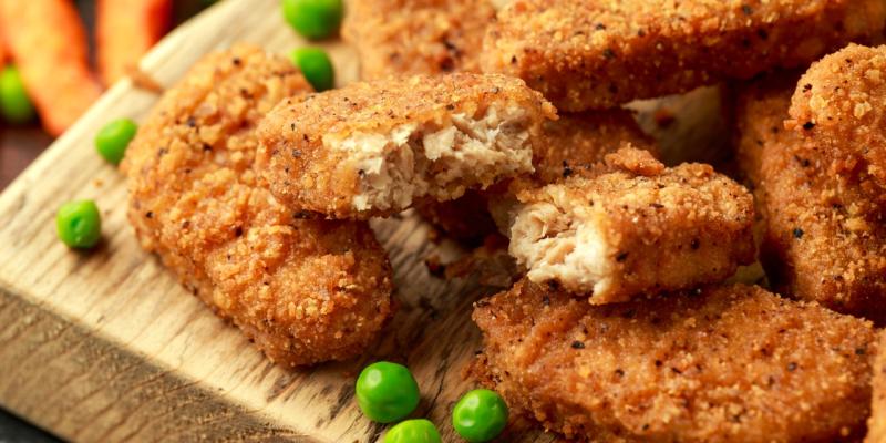 Vegane Nuggets neben Erbsen auf einem Holzbrett