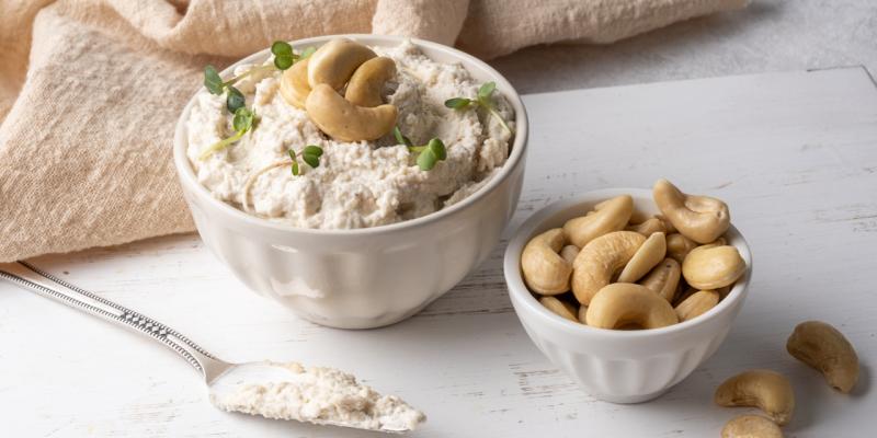 Frischkäse vegan in einer Schale, daneben eine Schüssel mit Cashewkernen