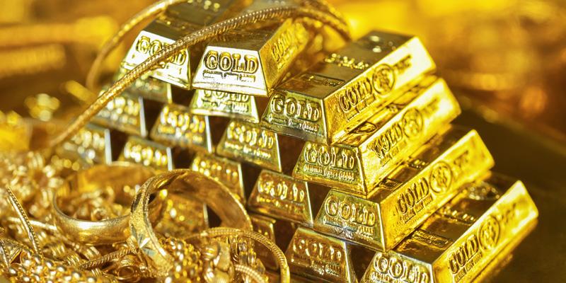 Gold kaufen - Edelmetall als Anlage: Gestapelte Goldbarren, davor verschiedenster Goldschmuck