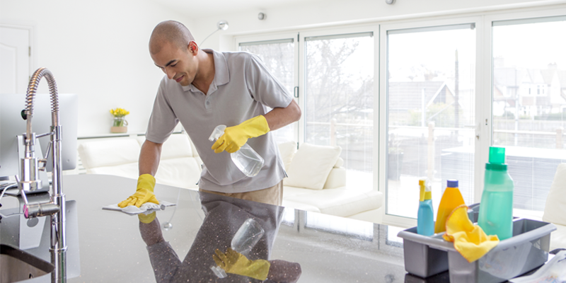 Kurzgeschorener Mann im grünen Polo und mit gelben Gummihandschuhen wischt hochglänzende Granitküchenplatte