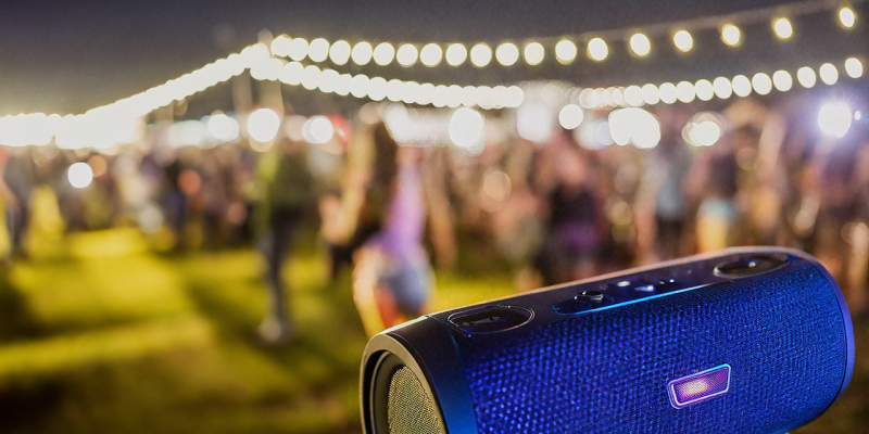 Hinten unscharf ein Freiluftfest bei Dunkelheit, vorne scharf ein Bluetooth Lautsprecher