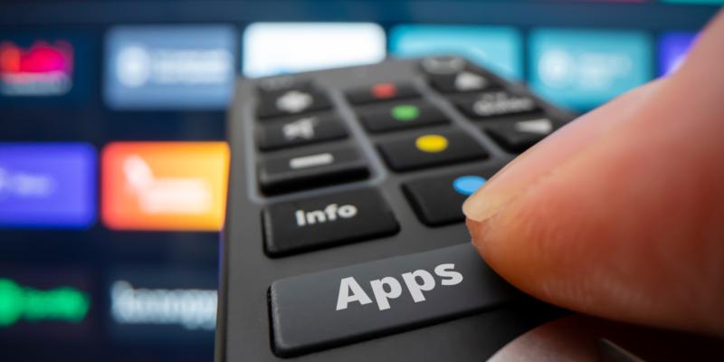 Jemand drückt auf einer Fernbedienung auf die Taste "Apps" und steuert damit einen Smart TV. 