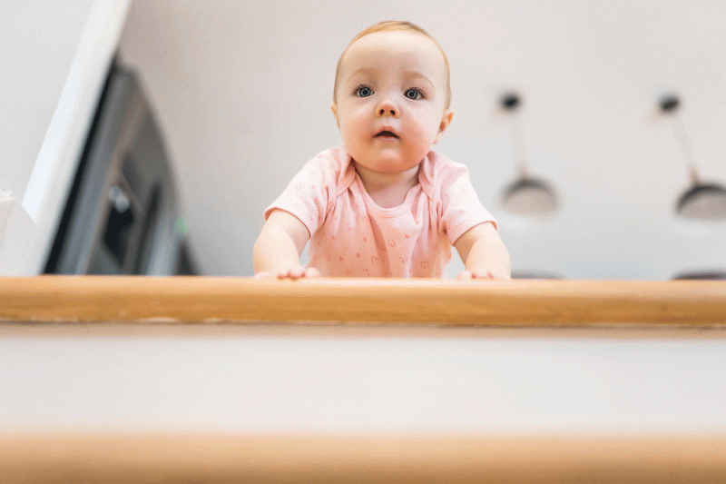 Hell und kurzärmliges Baby schaut krabbelnd frontal eine Treppe hinunter.
