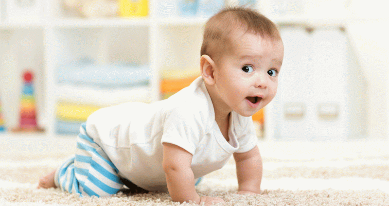 Auf hellem Teppichboden krabbelndes Baby mit kurzem, weißem Leiberl und blauweiß gestreifter Hose.