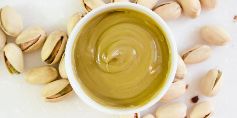 aus Vogelperspektive Pistaziencreme in einer weißen runden Schale auf weißem Untergrund inmitten von Pistazien in der Schale