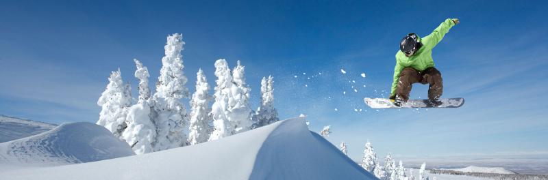 Snowboarder springt mit einer Hand am Brett (Grab) in tiefst verschneiter Winterlandschaft ins Blaue