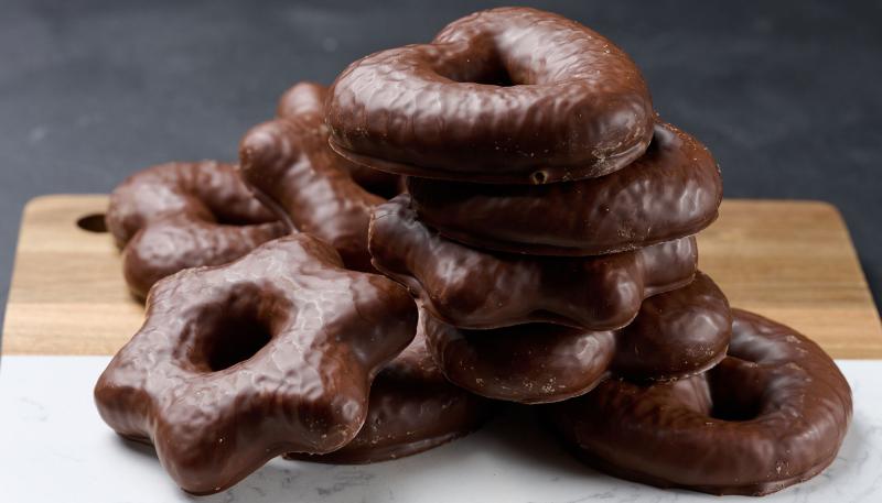 Übereinander liegende schokoladeüberzogene Lebkuchen auf hellem Untergrund und auf Holzbrett