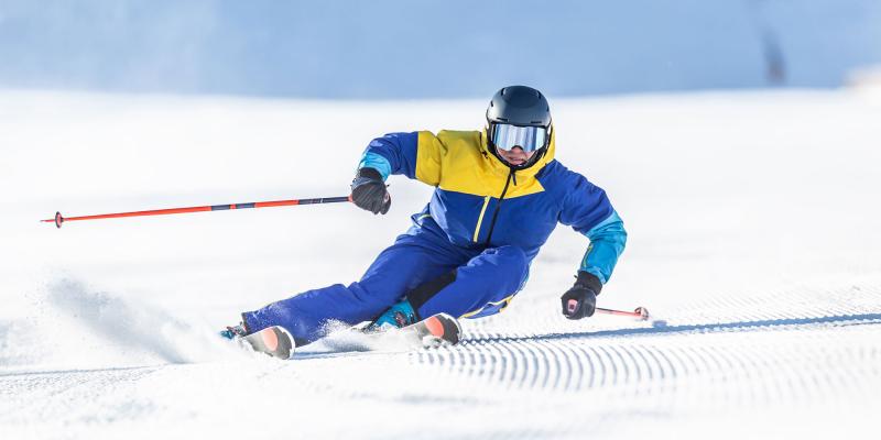 Skifahrer in Blau-Gelb carvt alleine bei Schönwetter auf Skipiste