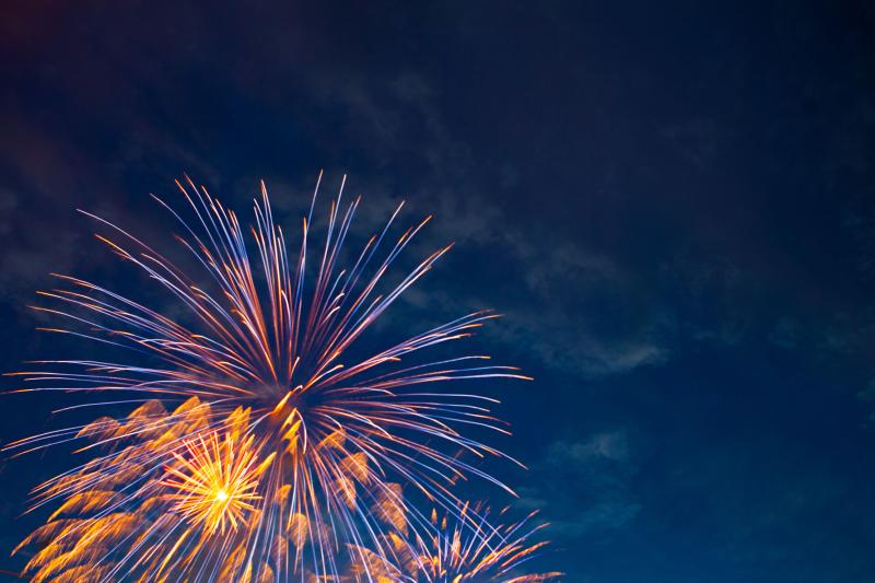 Feuerwerk in orange und blau-rot am Himmel, daneben Rauchschwaden