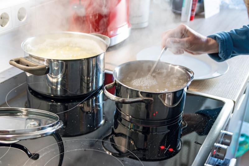 Induktionsherdplatte mit zwei Töpfen mit dampfendem Nudelwasser, in einem Topf rührt eine Hand um