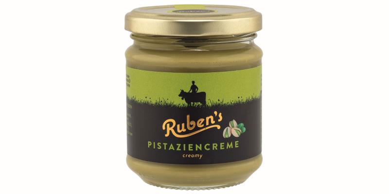 Ein rundes Glas „Ruben’s Pistaziencreme“ mit goldfarbenem Deckel. Die Creme ist hellgrün. Auf dem schwarzen Etikett stehen Markenname und „Pistaziencreme creamy“, daneben sind zwei Pistazien abgebildet. Oben ist eine grüne Wiese mit der Silhouette einer Person auf einem Pferd zu sehen.