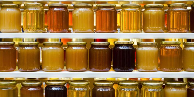 Viele Honiggläser mit unterschiedlich gefärbtem Honig in einem Regal