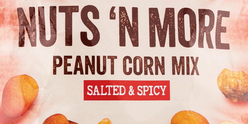 Die Auslobung auf der Packung Snack Fun Nuts 'n more Peanut Corn Mix in brauner und roter Schrift auf rotem und weißem Hintergrund. 