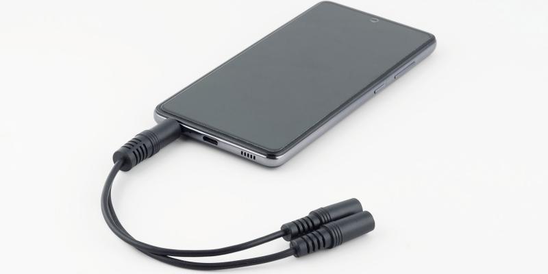 Smartphone mit eingestecktem Adapter, der aus einem Klinkenausgang zwei macht