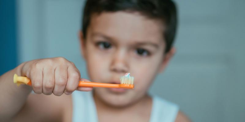 Bub hält waagrecht eine Zahnbürste mit einer kleinen Menge Pasta darauf