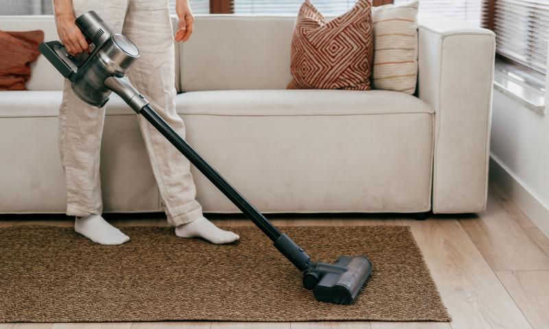 Mann saugt Teppich mit Akkustaubsauger