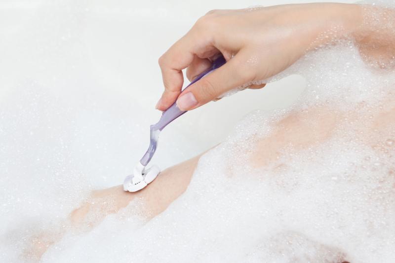 Damenbein wird im Schaum von Damenhand mit lila Nassrasierer rasiert
