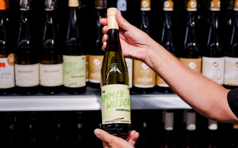 Mehrwegweinflasche vor einem vollen Weinregal im Handel