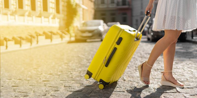 gelber kleiner Rollkoffer wird von Frau über Kopfsteinpflaster gezogen